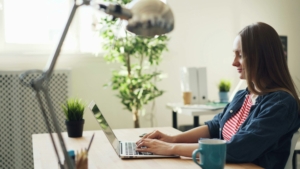 A white woman in an office, working on a laptop.