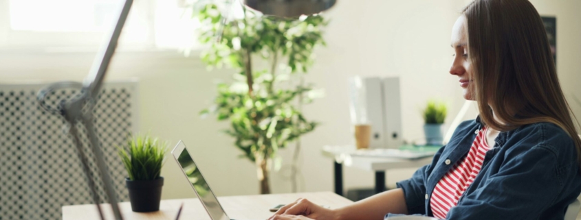 A white woman in an office, working on a laptop.