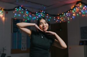 A woman with brown skin and hair, posing in front of a string of Christmas lights.