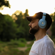 A bearded white man man wearing over the ear headphones outdoors.