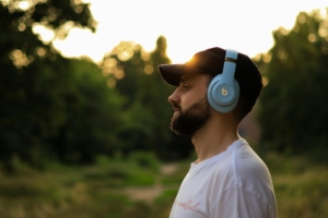 A bearded white man man wearing over the ear headphones outdoors.