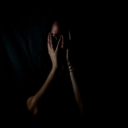 A person in the shadows holding their face in the dark.