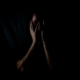 A person in the shadows holding their face in the dark.