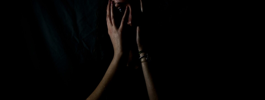 A person in the shadows holding their face in the dark.
