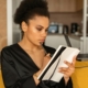 A Black woman thoughtfully writing in a notebook while sitting on a couch.