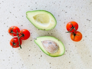 Tomatoes and an avocado on a countertop from above.