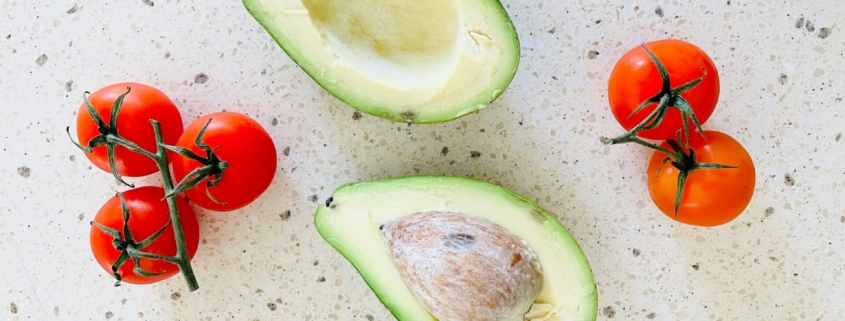 Tomatoes and an avocado on a countertop from above.