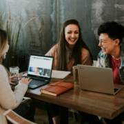 A group of young adults working on laptops at a table in a cafe.