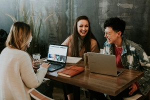 A group of young adults working on laptops at a table in a cafe.