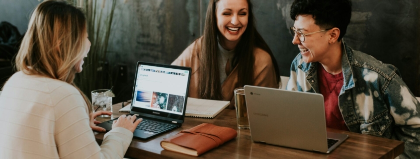 A group of young adults working on laptops at a table in a cafe.