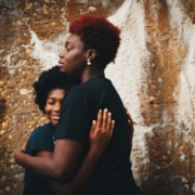 A Black mother hugging her Black teenage daughter.