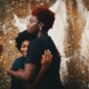 A Black mother hugging her Black teenage daughter.