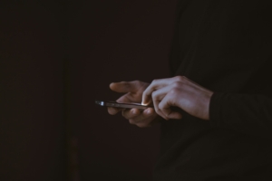 Disembodied hands holding a cell phone against a dark background.