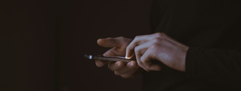 Disembodied hands holding a cell phone against a dark background.