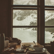 A view of a winter storm through a window, in front of which there is a cozy table with dishes from a meal.