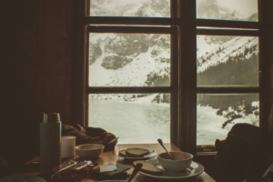 A view of a winter storm through a window, in front of which there is a cozy table with dishes from a meal.