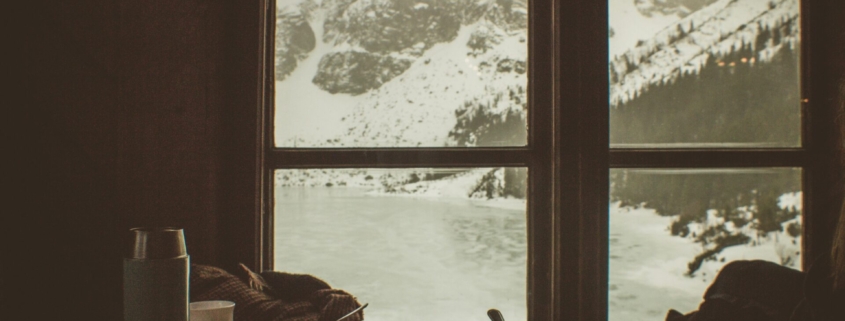 A view of a winter storm through a window, in front of which there is a cozy table with dishes from a meal.