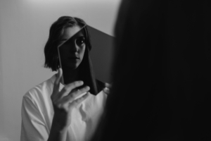 A woman staring through a transparent hexagon at her reflection in the mirror.