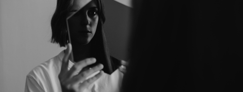 A woman staring through a transparent hexagon at her reflection in the mirror.