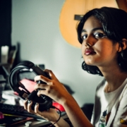 A teenage girl looking at the camera and holding a pair of headphones in her hands.