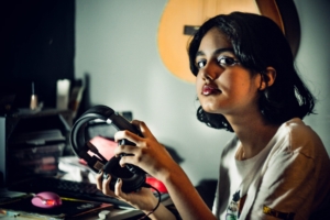A teenage girl looking at the camera and holding a pair of headphones in her hands.