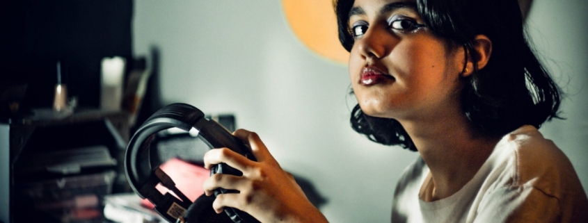A teenage girl looking at the camera and holding a pair of headphones in her hands.