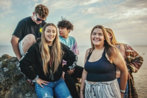 A group of teenagers smiling standing next to a body of water outside.