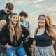 A group of teenagers smiling standing next to a body of water outside.