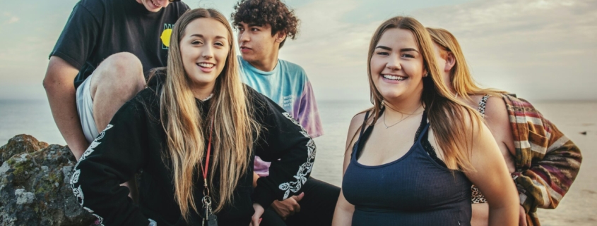 A group of teenagers smiling standing next to a body of water outside.