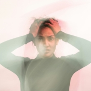 A hazy photo of a woman with brown skin holding her hands on her forehead, like she's distressed.