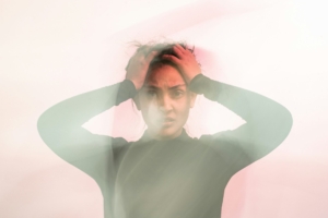 A hazy photo of a woman with brown skin holding her hands on her forehead, like she's distressed.