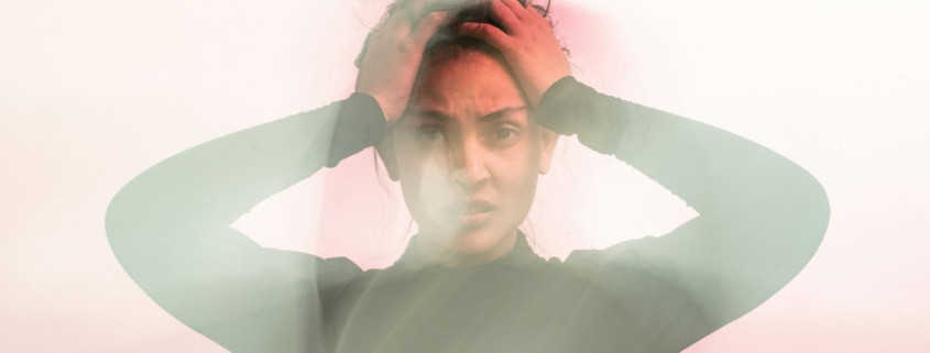 A hazy photo of a woman with brown skin holding her hands on her forehead, like she's distressed.