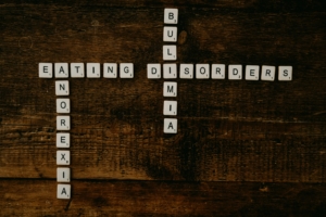 Scrabble tiles arranged to spell out the words 'eating disorder' horizontally and 'anoriexia' and 'bulimia' vertically on a dark wood surface.