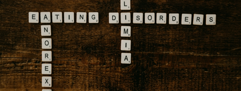 Scrabble tiles arranged to spell out the words 'eating disorder' horizontally and 'anoriexia' and 'bulimia' vertically on a dark wood surface.