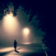 A silhouette of a person walking under a streetlight.