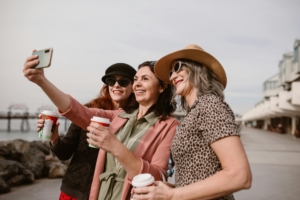A group of middle aged women taking a selfie outside while holding coffee.