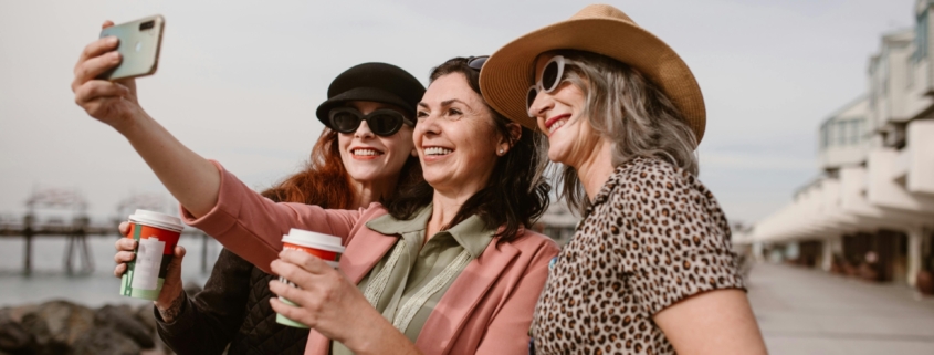A group of middle aged women taking a selfie outside while holding coffee.