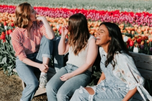 A group of women laughing on a bench next to a colorful field of tulips.