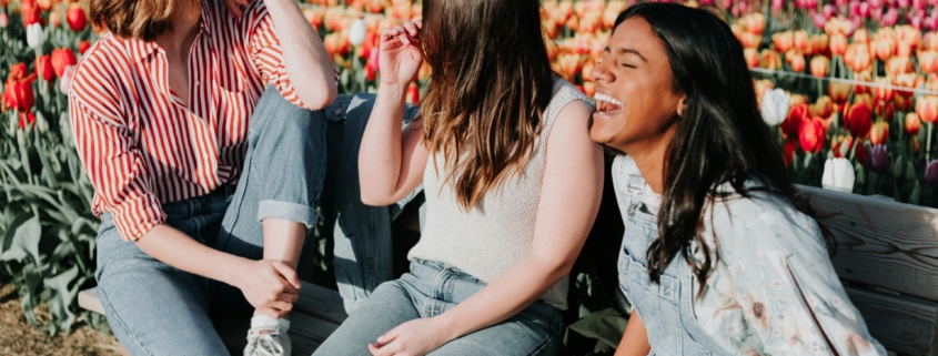 A group of women laughing on a bench next to a colorful field of tulips.