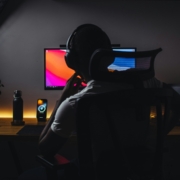 A person, from behind, sitting at a computer in a dark room.