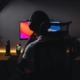 A person, from behind, sitting at a computer in a dark room.
