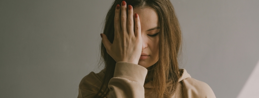 A white woman holding her hand up to her face, looking upset.