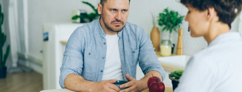 An frowning man sitting at a table across from a woman.