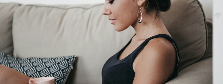 A woman sitting on a couch, looking down at a mug in her hands