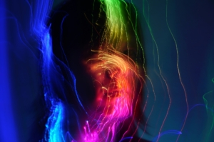 A silhouette of a person with long hair with colorful bands of light over their face.