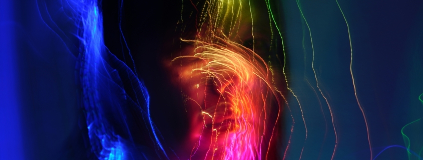 A silhouette of a person with long hair with colorful bands of light over their face.