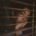 A sad looking young woman looking out a window through the open blinds.