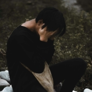 A person sitting outside with their head in their hands, looking upset.