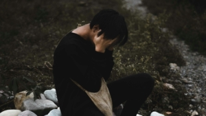 A person sitting outside with their head in their hands, looking upset.