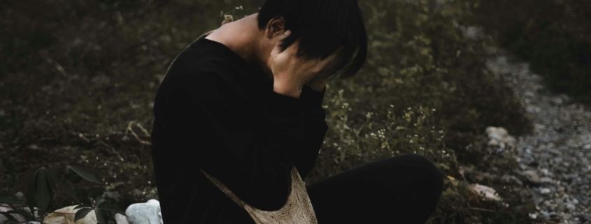 A person sitting outside with their head in their hands, looking upset.